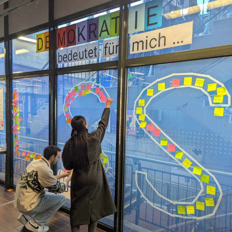 Schülerin klebt einen Zettel um zu zeigen, was für sie Demokratie bedeutet