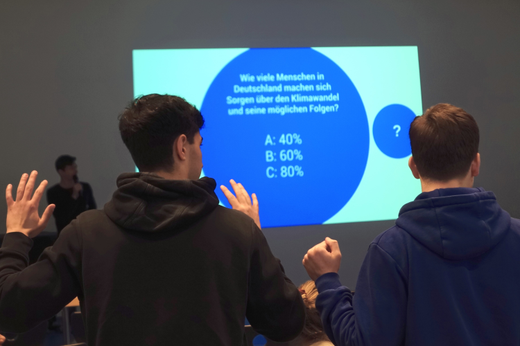 Zu sehen sind zwei Schüler, die sich melden zu der Frage, wie groß der Anteil der Menschen in Deutschland ist, die sich Sorgen über den Klimawandel und seine Folgen machen.